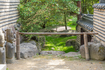 A bamboo bar gate marks the entrance between stone walls. Guardian statues add cultural significance.