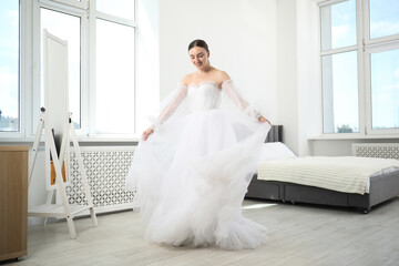 Dreams come true. Woman wearing beautiful wedding dress looking at herself in mirror indoors