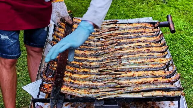Grilled fish being prepared outdoors on a barbecue by a person in gloves