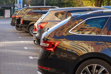 Obraz premium Several parked cars in a row show reflections of surrounding buildings under clear skies in a bustling urban setting