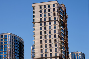 Fototapeta premium A modern apartment building stands tall with many windows. Other apartment buildings appear alongside under a clear blue sky in a cityscape