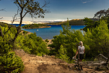 A woman sits on a bench in the middle of a forest, with a panoramic view of Strucic Beach on the...