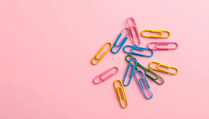 Pastel pink surface featuring colorful paper clips scattered randomly in flat lay creative design