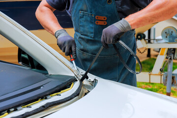 Technician works meticulously on windshield of car, using tools to remove old sealing material.