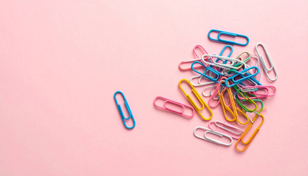 Flat lay pastel pink background with randomly scattered colorful paper clips creative office supplies