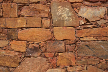 Fototapeta premium Rustic Stone Wall Texture in Leon, Spain: a close-up of a rustic, weathered stone wall with irregular shapes and a mix of reddish-brown and gray colors, a natural pattern and texture.