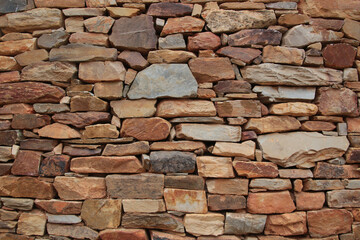Rustic Stone Wall Texture in Leon, Spain: a close-up of a rustic, weathered stone wall with irregular shapes and a mix of reddish-brown and gray colors, a natural pattern and texture.