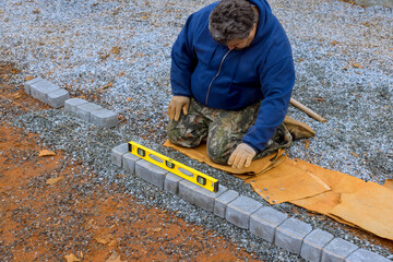 Worker is carefully lining up gray bricks using level tool at construction site.