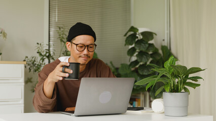 Asian man drinking morning coffee while working at home.