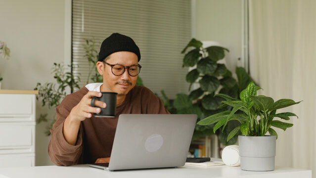 Asian man drinking morning coffee while working at home.