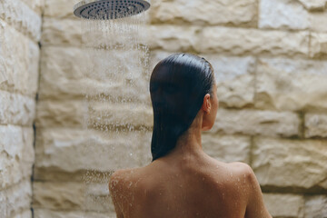 Woman enjoying outdoor shower with stone wall background, wet hair, and water droplets cascading...