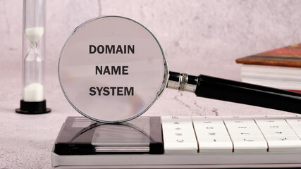 A magnifying glass highlights the term Domain Name System placed on a modern calculator, alongside an hourglass, symbolizing time and technology in a studied environment