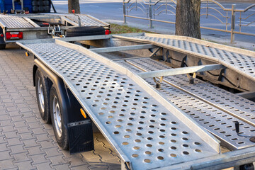 Obraz premium A trailer with a metallic surface is parked on a tree-lined street in the early morning light, emphasizing its functional design and construction