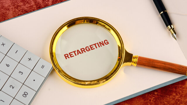 A magnifying glass highlights the word retargeting on paper, accompanied by a calculator and a pen, symbolizing marketing strategy and analytics analysis