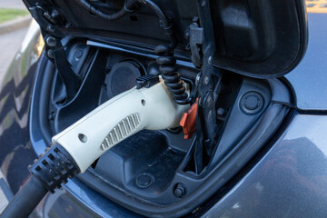 Close-up view of an electric vehicle's charging port with a connector attached in a city setting on...