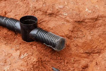 Workers prepare trench for drainage pipe installation amid red soil, construction debris in urban...
