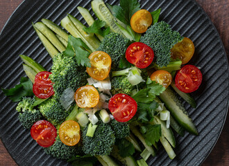 Plate of chopped broccoli, cucumbers and cherry tomatoes with fresh herbs