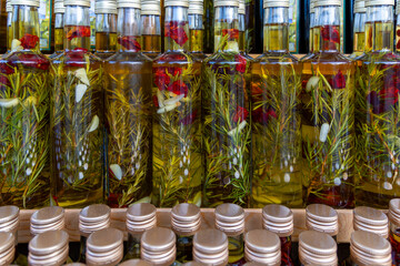 Bottles of infused olive oil with herbs and spices. Close-up of glass bottles filled with olive oil infused with rosemary, garlic, and dried chili peppers, displayed for sale.