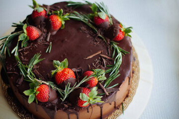Chocolate cake with ganache drip topped with strawberries and rosemary wreath