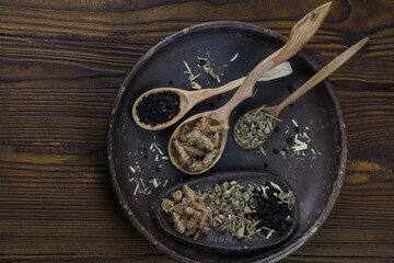 Dark ceramic bowl with wooden spoons holding dried herbs and berries