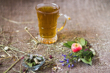 Warm herbal drink with apple and flowers on rustic burlap surface