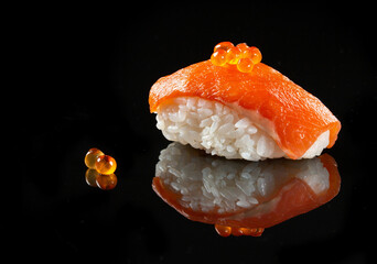 Close-up of salmon nigiri sushi with salmon roe garnish on black surface
