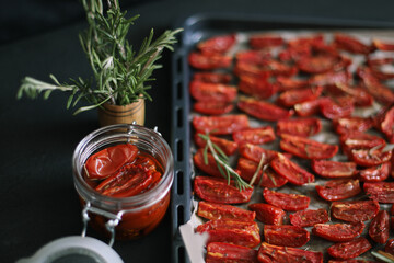 Baking sheet with halved tomatoes prepared for drying with rosemary