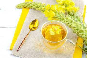Glass cup of mullein herbal tea on natural wooden background with fresh Verbascum thapsus flowers