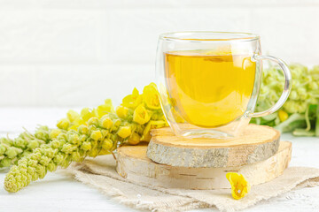 Glass cup of mullein herbal tea on natural wooden background with fresh Verbascum thapsus flowers