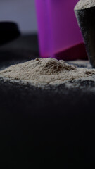 Protein powder spread on a black surface with a pink shaker placed in the background, representing...