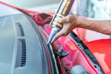 A hand is using a glass sealant to apply adhesive along the edge of a car's windshield. Fixing or...
