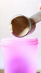 Scoop filled with protein powder being poured into a protein shaker, representing fitness, nutrition, and healthy lifestyle preparation.