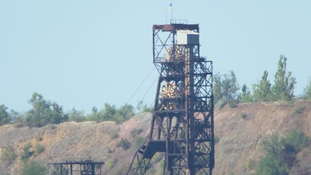 Mining headframe with large rotating wheels on hot summer day in Ukraine. Heatwave creates shimmering mirage effect, illustrating impact of global warming