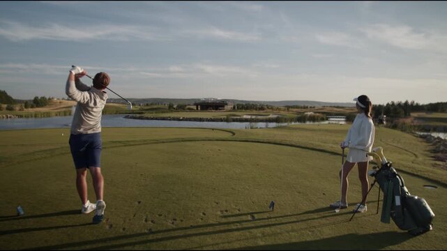 Man golfer trains golf swing on green course as woman watches