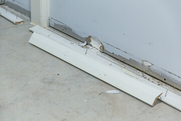 Construction debris from broken white baseboards and damaged wall along floor during interior...