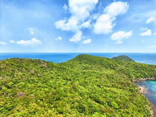 Fototapeta premium Lush green hills meet serene blue ocean under a vibrant sky at a tropical coastal location