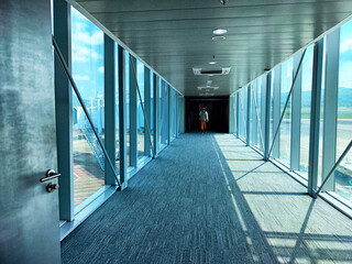 Long airport corridor leading to the boarding area with natural light streaming in and a traveler...