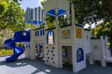 Colorful playground with a blue slide, climbing wall, and castle-like structure, surrounded by lush...