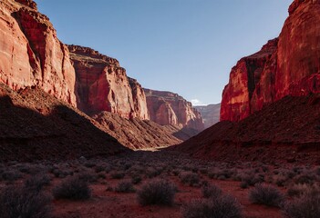 Fototapeta premium A breathtaking view of a vast canyon with towering red rock formations and sparse desert vegetation under a clear blue sky
