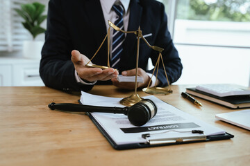 A professional lawyer in a suit works on a laptop with legal documents, gavel, money, and scales of justice on desk.