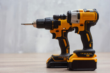 A cordless drill and an impact driver rest on a wooden surface. Tools for construction or DIY projects in a workshop setting.
