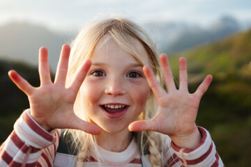 Child girl showing hands counting her fingers happy smiling face 5 years old kid travel outdoor looking at camera close up, family travel vacations candid emotions
