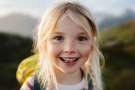 Child girl happy smiling face 5 years old kid hiking with backpack outdoor portrait looking at camera close up blonde hair family travel vacations candid emotions - Powered by Adobe