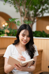 Young woman  sitting at table in coffee shop and makes notes in notebook writing down general ideas...