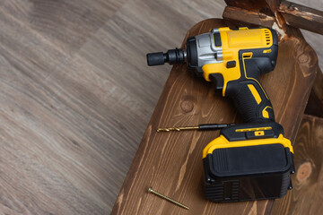 Naklejka premium Yellow and black cordless impact driver with battery on wooden planks alongside drill bits. Professional construction power tool for woodworking.