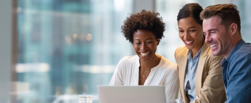 The team of diverse professionals collaborating happily around a laptop in modern office