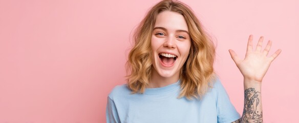 The young woman waving and laughing in a pastel pink studio portrait with tattooed arm