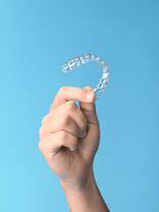 Hand holding a clear dental aligner on a blue background in studio shot