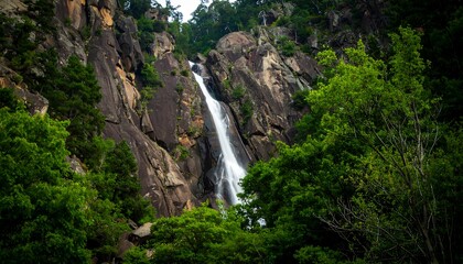 Waterfall cascading down rocky cliff face surrounded by lush greenery