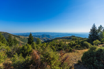 Scenic mountain landscape featuring rolling forested hills under clear blue sky